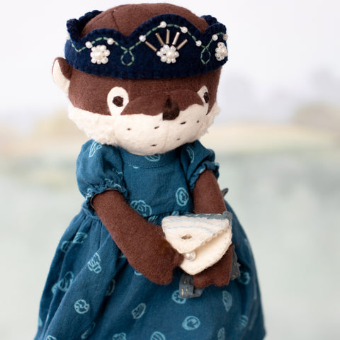 clara otter wearing riverbank dress and riverine queen crown, holding shell pouch